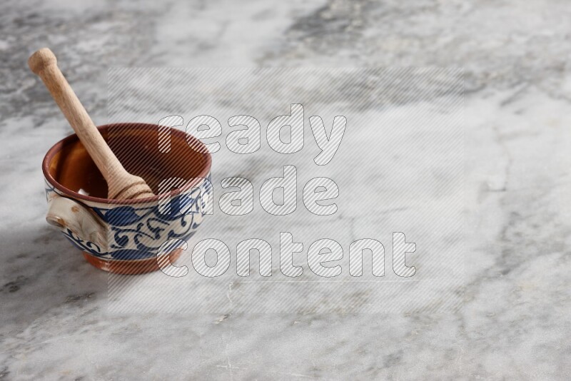 Decorative pottery pot with wooden honey dipper in it on grey marble background