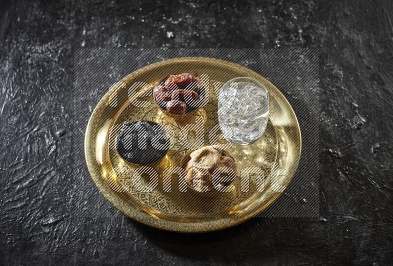 Dried fruits in metal bowls with water on a tray in dark setup