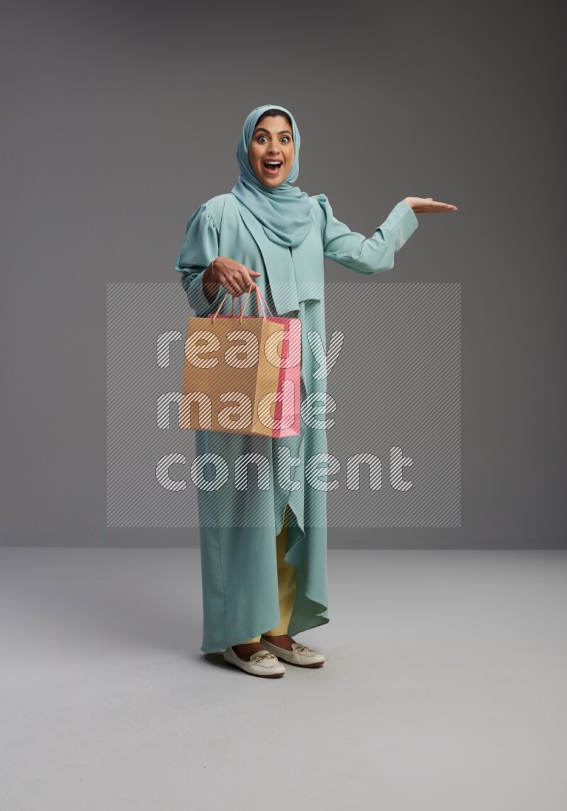 Saudi Woman wearing Abaya standing holding shopping bag on Gray background