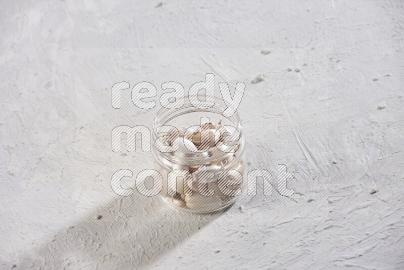 A glass jar full of garlic cloves on a textured white flooring