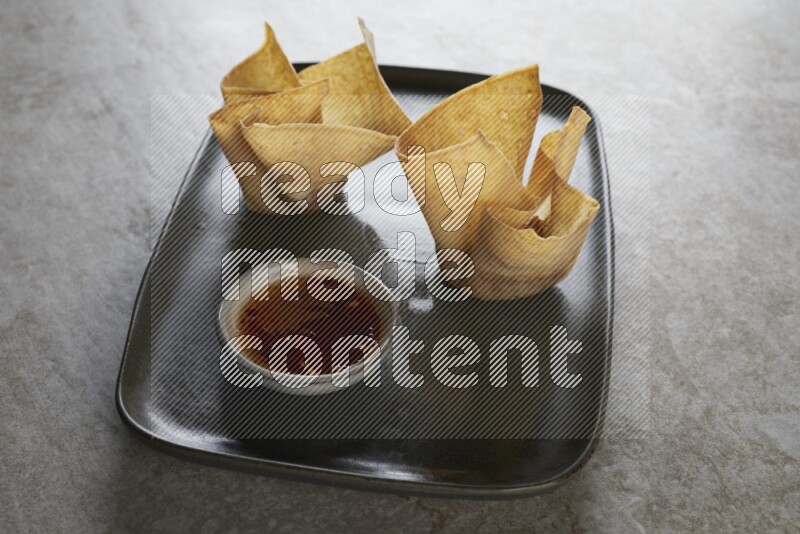 wonton cups with soy sauce ramkin on rectangle dark grey ceramic plate on grey textured counter top
