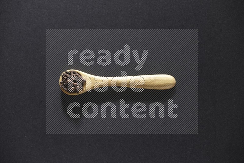 حبوب القرنفل في ملعقة خشبية علي خلفية سوداء