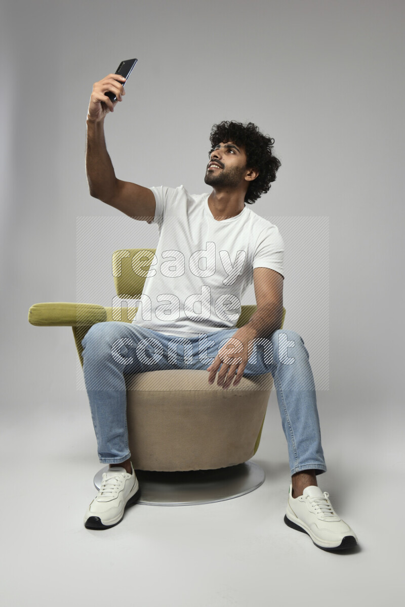 A man wearing casual sitting on a chair taking a selfie on white background