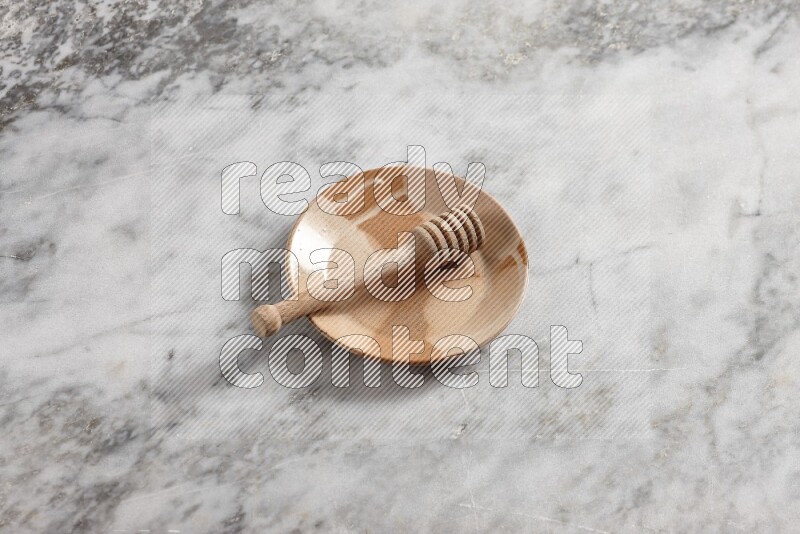 Multicolored pottery plate with wooden honey dipper in it on grey marble background