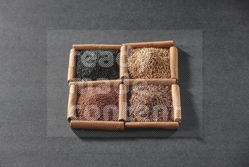 4 squares of cinnamon sticks full of flaxseeds, garden cress, black seeds and mustard seeds on black flooring