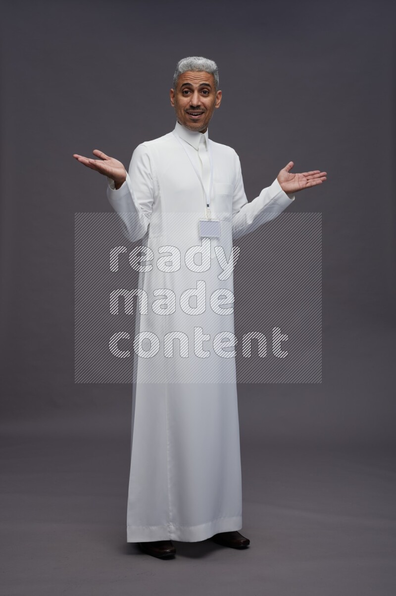 Saudi man wearing thob with neck strap employee badge standing interacting with the camera on gray background
