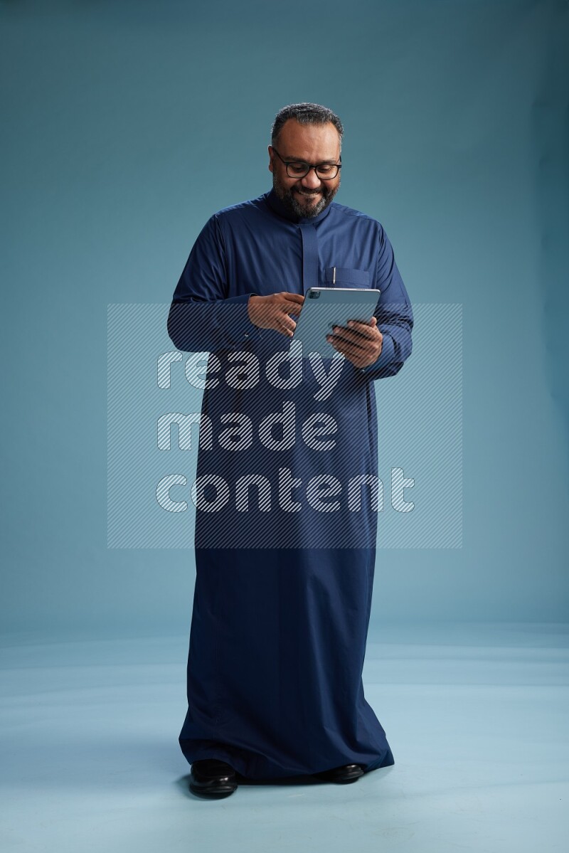 Saudi Man without shimag Standing working on tablet on blue background