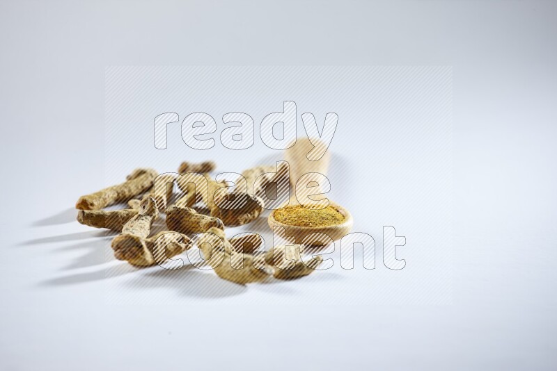 A wooden spoon full of turmeric powder with dried turmeric fingers beside it on white flooring