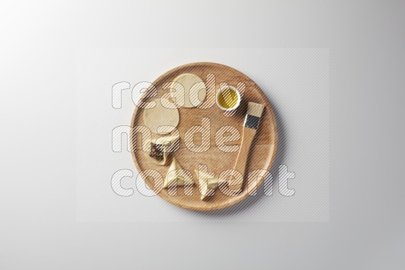 two closed sambosas and one open sambosa filled with meat while oil with oil brush aside in a wooden dish on a white background