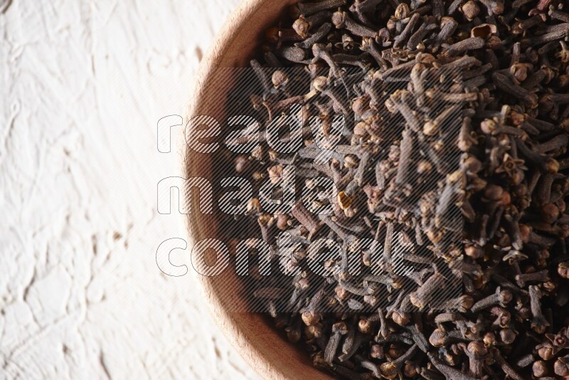 A wooden bowl full of cloves on a white flooring