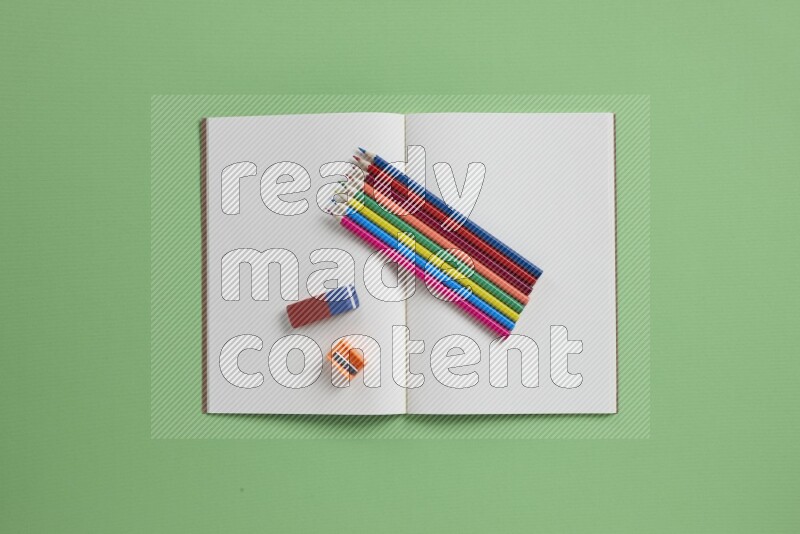 A blank open notebook with different school supplies on green background