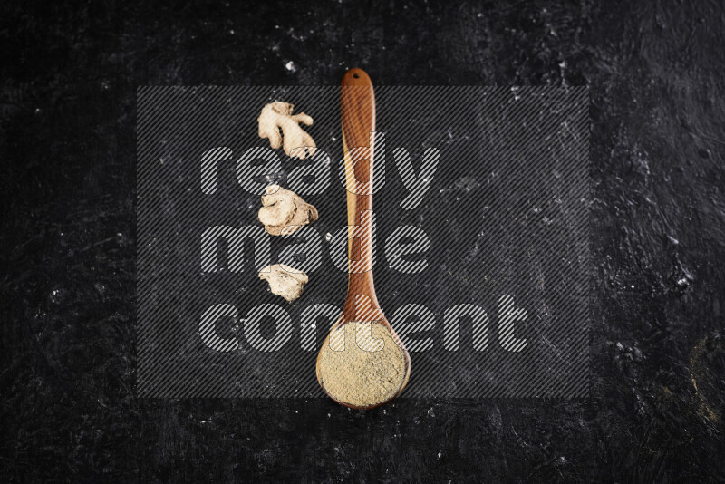 A wooden ladle full of ground ginger powder on black background