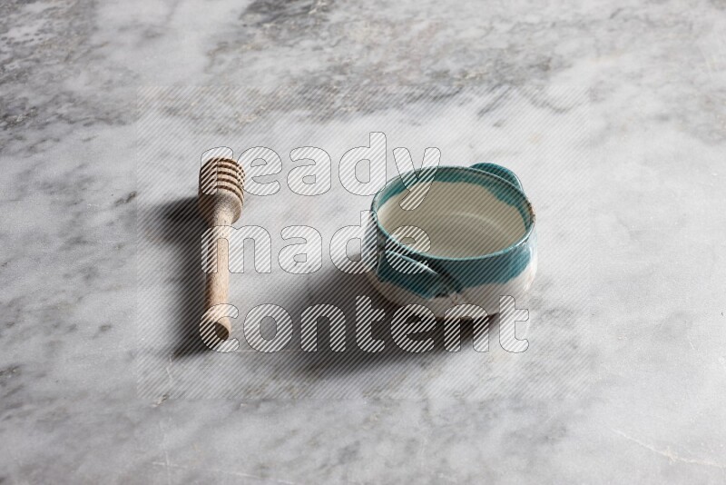 Multicolored pottery bowl with wooden honey dipper on the side on grey marble background
