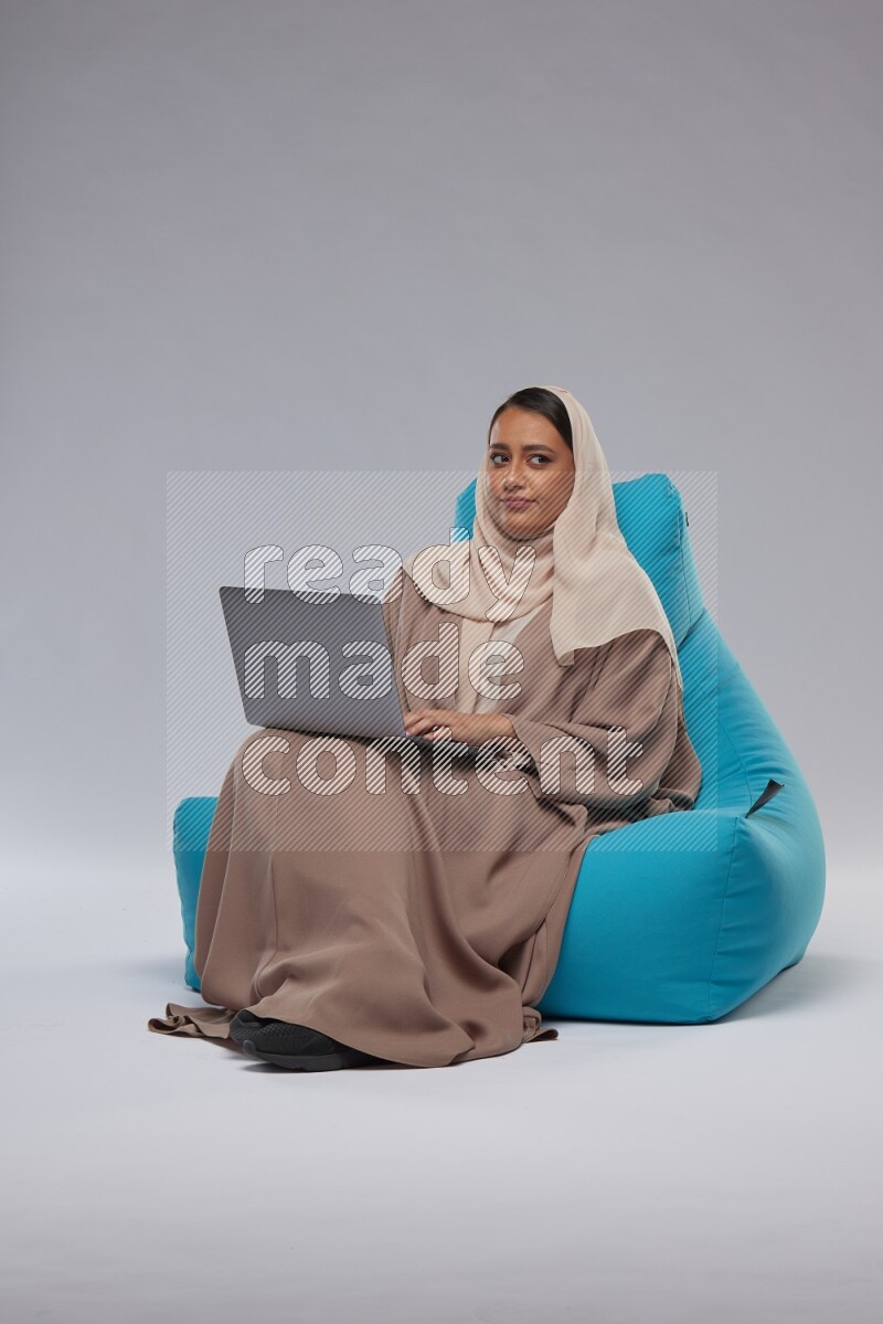A Saudi woman sitting on a blue beanbag and working on laptop