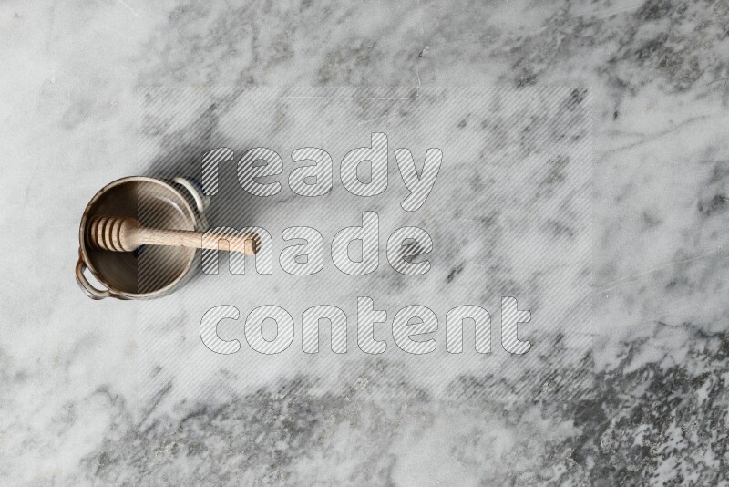 Multicolored pottery bowl with wooden honey dipper in it on grey marble background
