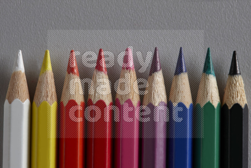 A collection of colored pencils arranged showcasing a gradient of different hues on grey background