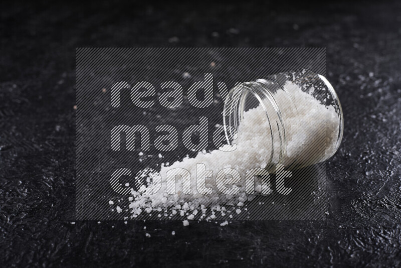 A glass jar full of coarse sea salt crystals on black background