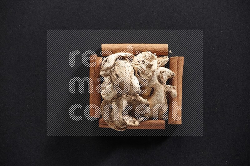 A single square of cinnamon sticks full of dried ginger on black flooring