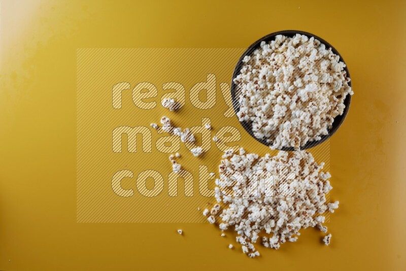 A copper ceramic bowl full of popcorn with popcorn beside it on a yellow background in different angles