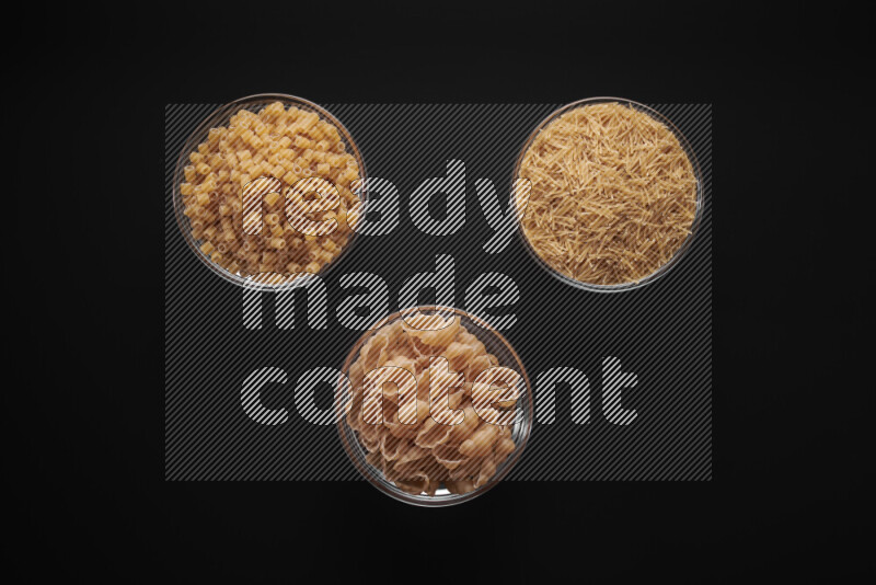 Different pasta types in glass bowls on black background