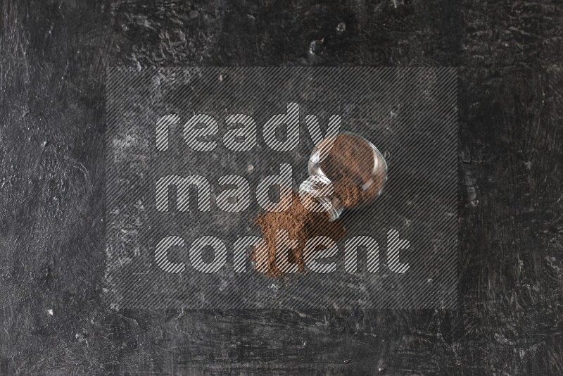 وعاء زجاجي للتوابل مقلوب ممتلئ ببودرة القرنفل والبودرة سقطت منه على أرضية سوداء