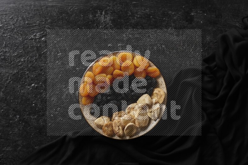 Dried fruits in a pottery bowl with nuts in a dark setup