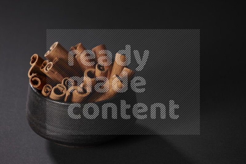 Cinnamon sticks in a black bowl on a black background in different angles