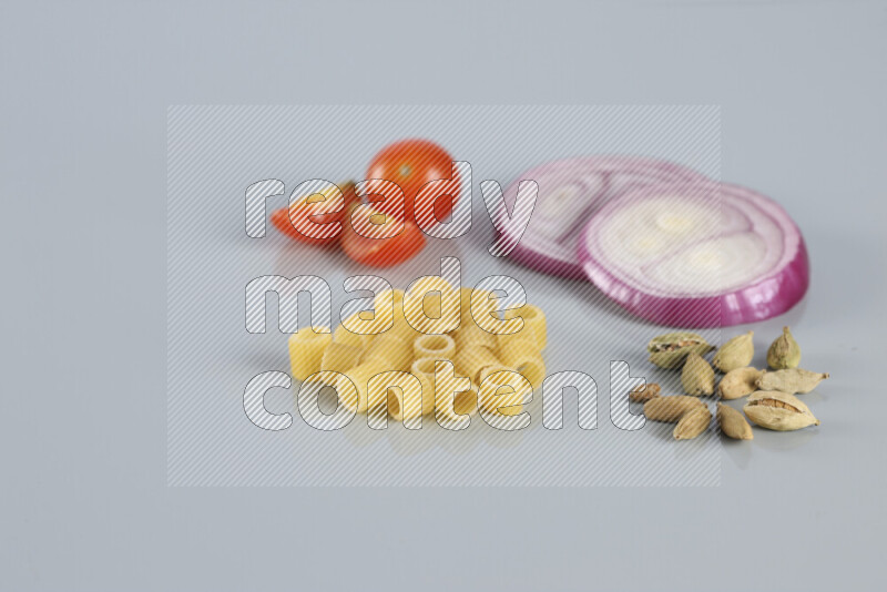 Raw pasta with different ingredients such as cherry tomatoes, garlic, onions, red chilis, black pepper, white pepper, bay laurel leaves, rosemary, cardamom and mushrooms on light blue background