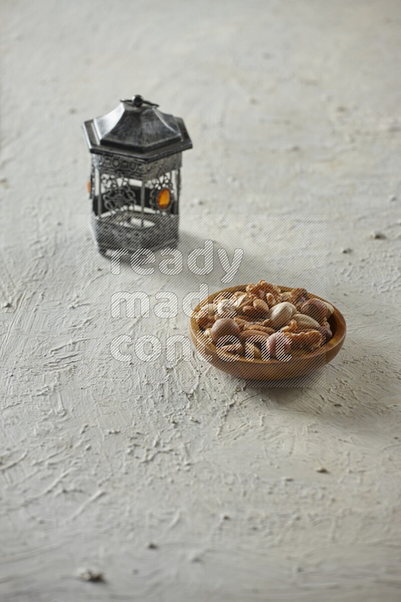 A silver lantern with different drinks, dates, nuts, prayer beads and quran on textured white background