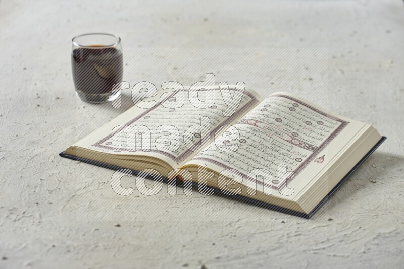 Quran with dates, prayer beads and different drinks all placed on textured white background