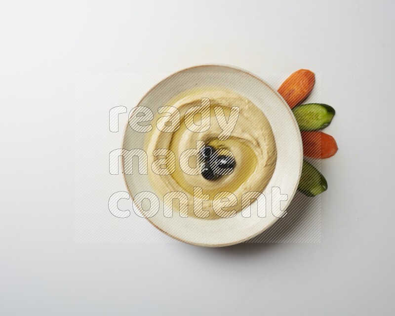 Hummus in a pottry plate garnished with black olives on a white background