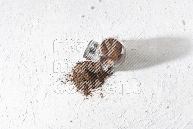 وعاء زجاجي مقلوب ممتلئ ببودرة القرنفل وتناثرت البودرة منه على أرضية بيضاء