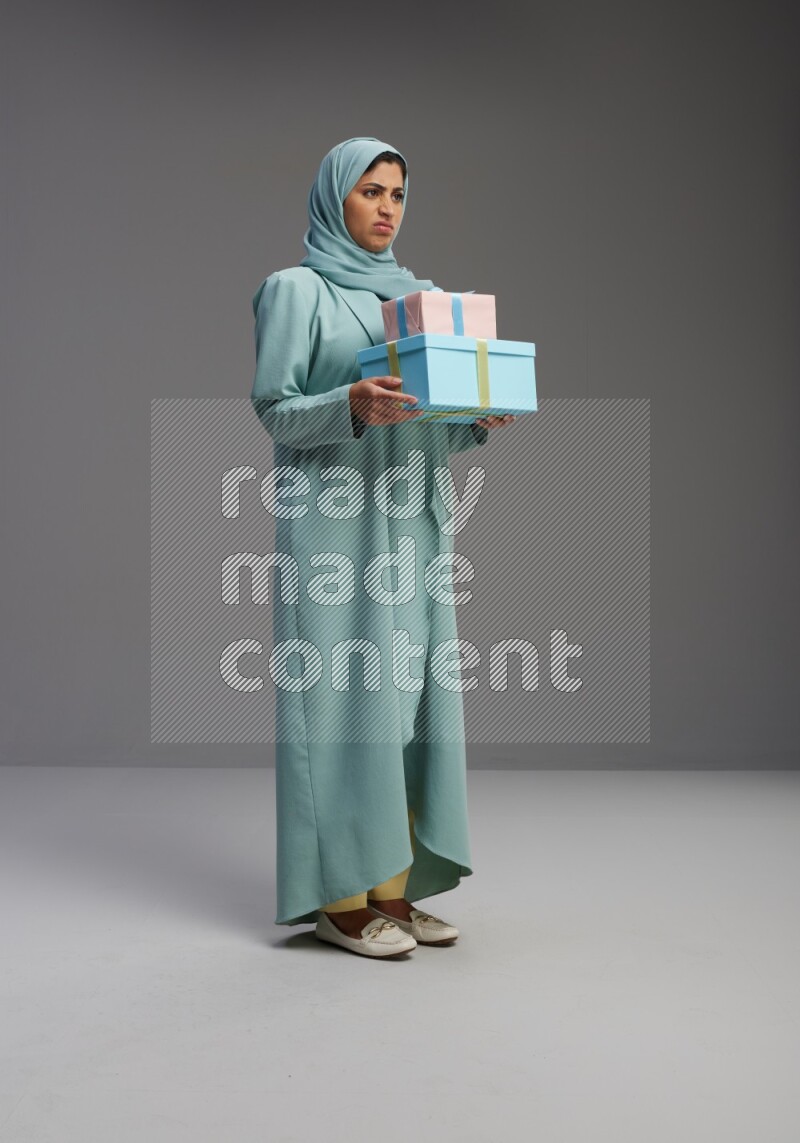 Saudi Woman wearing Abaya standing holding gift box on Gray background