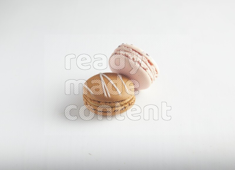 45º Shot of of two assorted Brown Irish Cream, and pink orange blossom macarons on white background