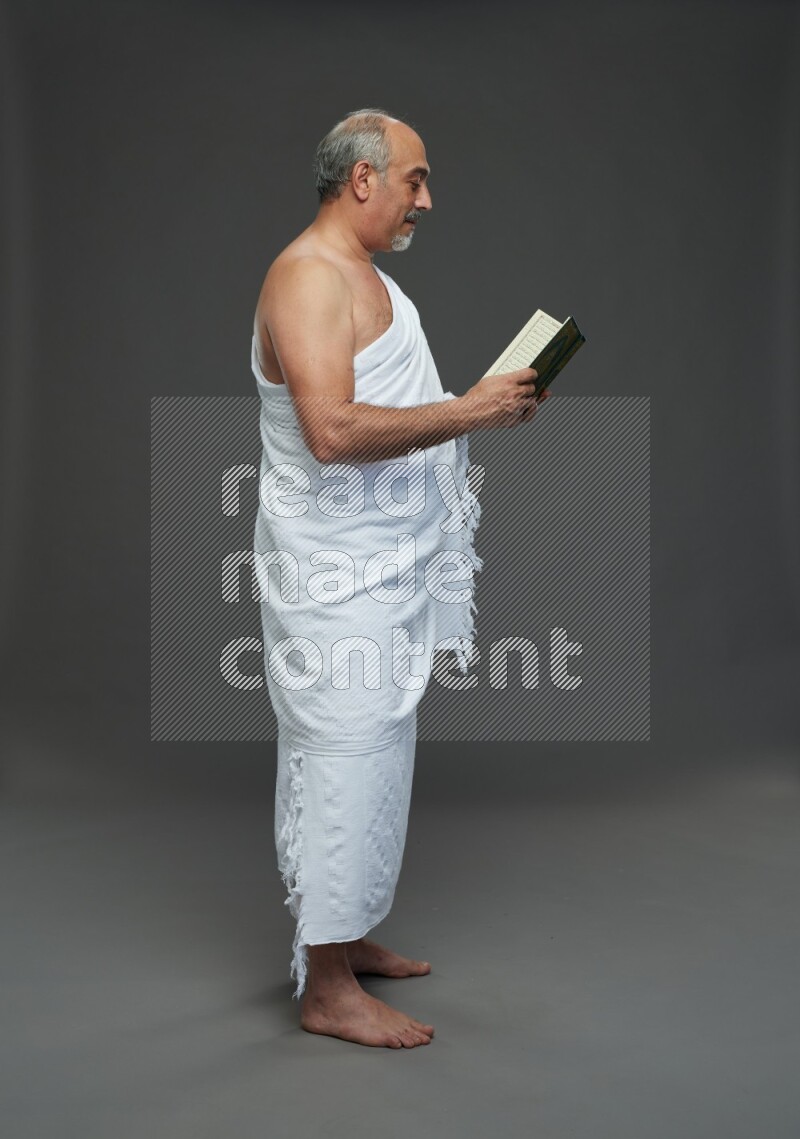 A man wearing Ehram Standing reading quran on gray background