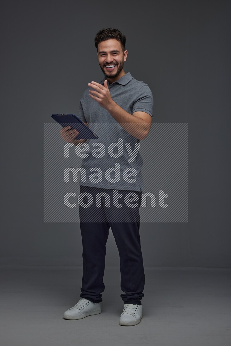 A man wearing casual standing and using his tablet and making multi hand gestures different angles eye level on a gray background