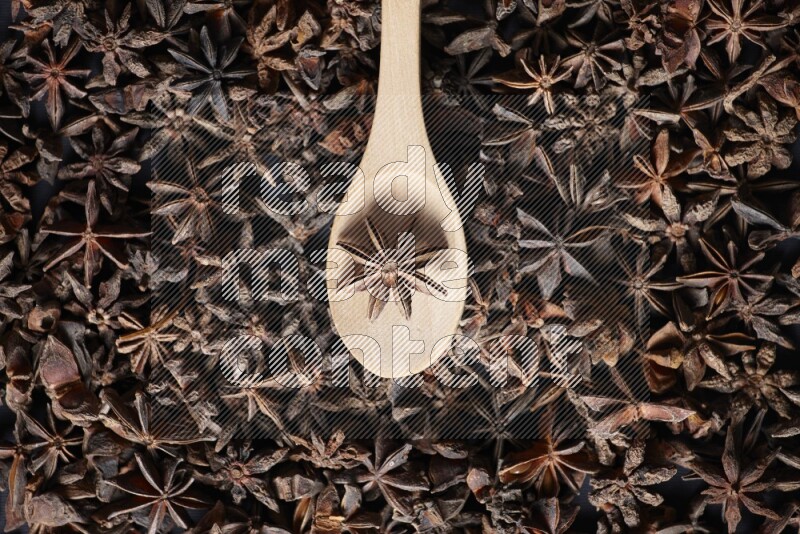 Star Anise in a wooden spoon on more stars anise filling the frame on black flooring