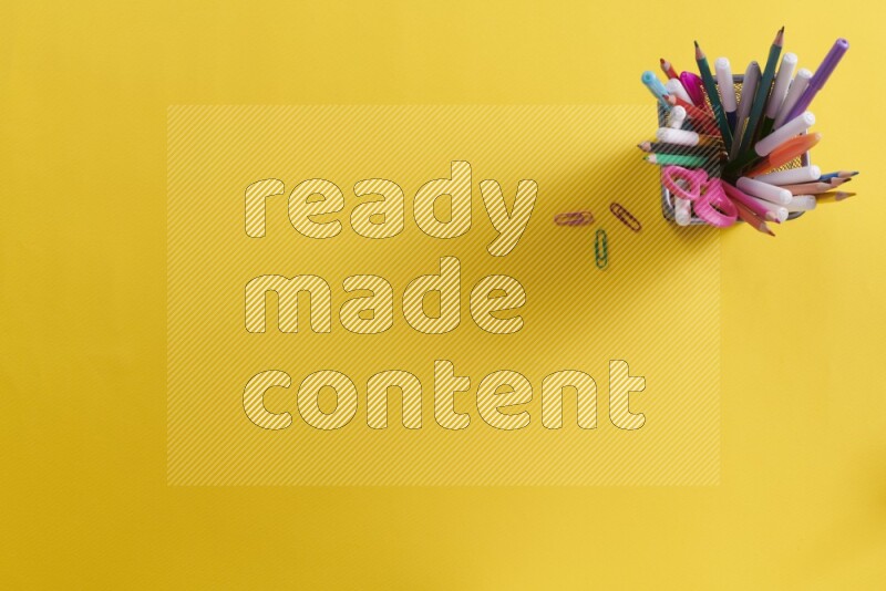 بعض الأقلام والمستلزمات المدرسية في مقلمة معدنية علي خلفية صفراء