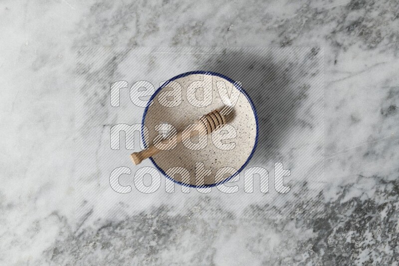 Multicolored pottery bowl with wooden honey dipper in it on grey marble background