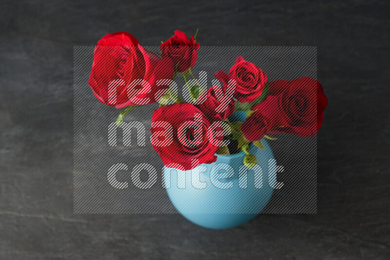 An arrangement of vivid red roses in a blue vase on black marble background