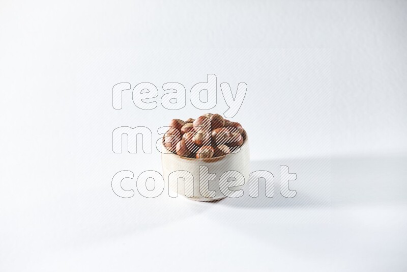 A beige ceramic bowl full of hazelnuts on a white background in different angles