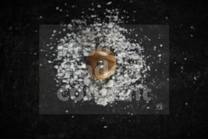 A wooden grinder standing upright and surrounded by coarse white sea salt on black background