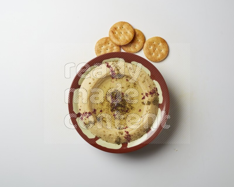 Hummus in a traditional plate garnished with zaatar & sumak on a white background