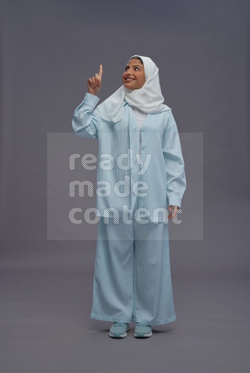 Saudi woman wearing hijab clothes standing interacting with the camera on gray background