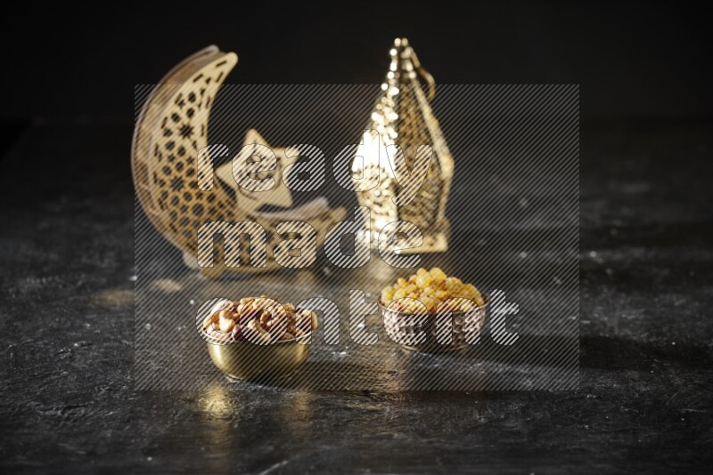 Nuts in a metal bowl with raisins beside golden lanterns in a dark setup