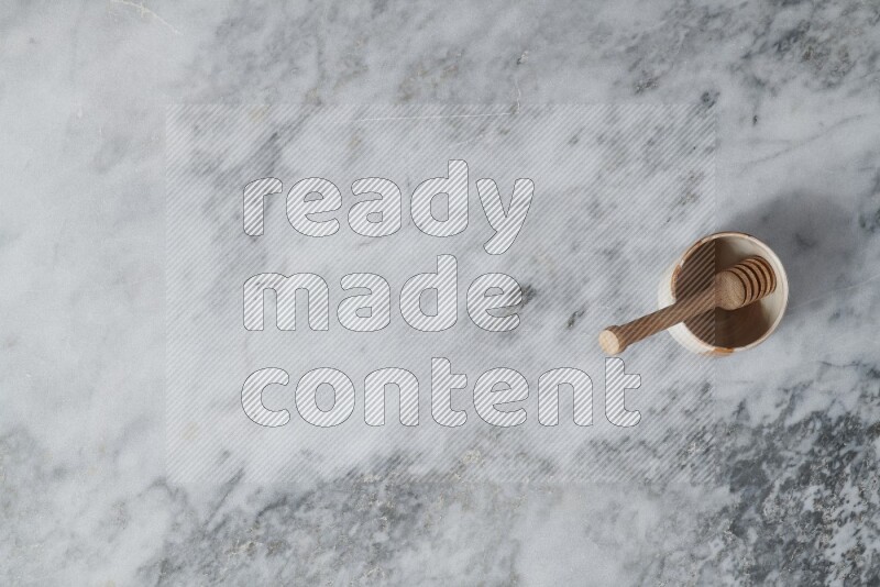 Multicolored pottery bowl with wooden honey dipper in it on grey marble background