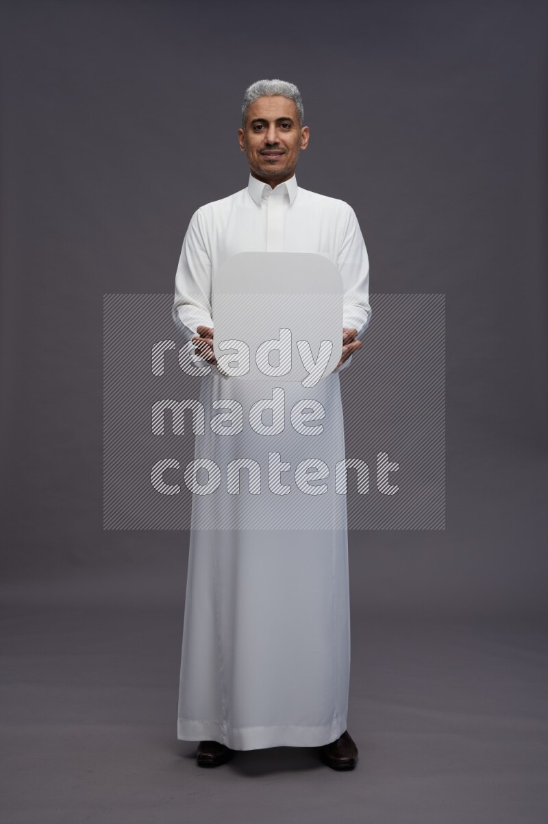Saudi man wearing thob standing holding social media sign on gray background