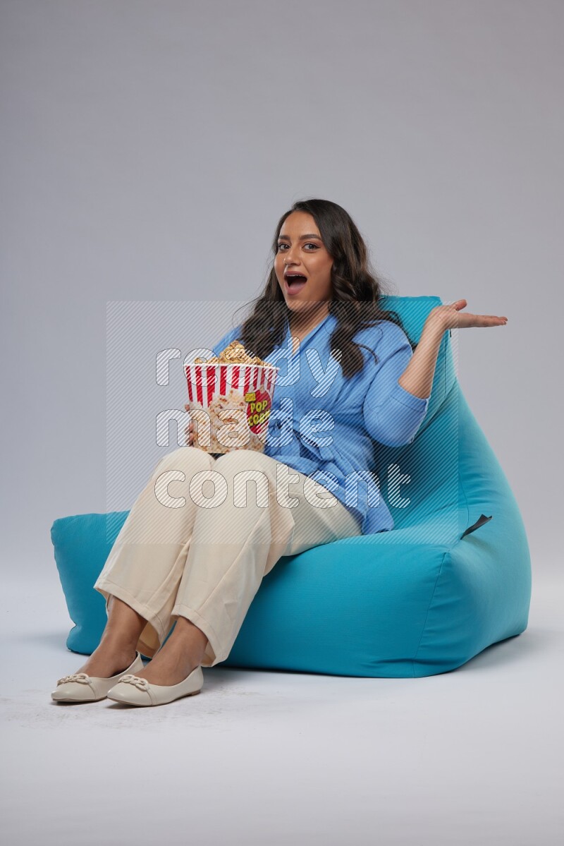 A woman sitting on a blue beanbag and eating popcorn