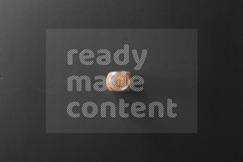 A glass spice jar full of mustard seeds on black flooring