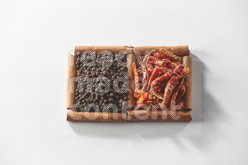 مربعان من أعواد القرفة ممتلئان بالفلفل الحار المجفف وحبوب الفلفل الأسود علي خلفية بيضاء